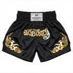 Black Muay Thai shorts with gold and white designs on a white background