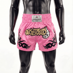 Pink boxing shorts with black and gold designs on a mannequin against a white background