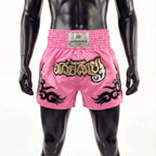 Pink boxing shorts with black and gold designs on a mannequin against a white background